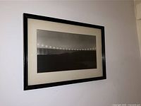Framed black and white photography art piece with a simple black frame and white matting showing a minimalist landscape with lights and horizon line.