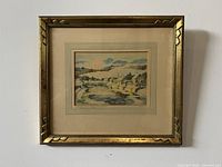 Framed watercolor painting showing full artwork and matting in gold-tone frame hung on wall.