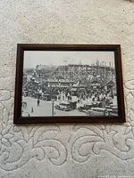 Framed black and white photo of a crowded amusement park scene with wooden roller coaster and vintage cars.