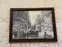 Framed black and white photo showing busy city intersection with vintage streetcars, cars and pedestrians in 1938 Toronto