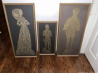 Photo showing the three framed brass rubbing artworks arranged on wooden floor against the wall.