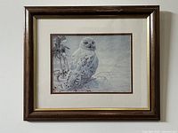 Framed snowy owl art print with muted winter background and white matboard in dark brown wood frame.