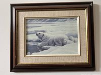 Framed artwork showing polar bear and cubs resting on ice, beige mat, dark wood and gold frame.