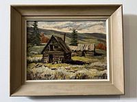 Framed oil painting of a deserted homestead with two wooden cabins in a natural outdoor setting.