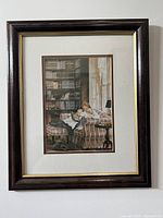 Framed print of woman reclining on sofa reading, dark wood frame and cream matting, shows bookstore background