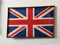 Framed vintage Great Britain (Union Jack) flag mounted on a wooden board with visible wood grain frame against a white wall.