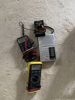 Photo of the BK Precision tester, two multimeters, and a small electronic testing device all laid on a carpet.