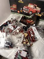Two identical LEGO pickup truck sets at least partially assembled, bags of LEGO bricks in varying colors (primarily dark red, black, cream), four LEGO tires, two printed instruction manuals, and original boxes featuring red pickup truck models.