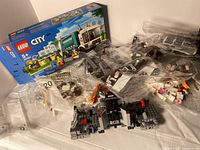 Overview of Lego City garbage truck set components including original box and multiple bags of pieces, three small built toys visible.