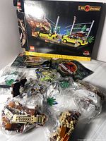 Photo showing partially assembled LEGO pieces and original box with Jurassic Park T. rex Breakout graphics, along with bags of LEGO components.