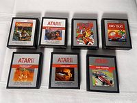 Photo showing seven Atari 2600 game cartridges laid on white surface with titles visible including Jungle Hunt, E.T., Crystal Castles, Dig Dug, Swordquest Earthworld, Vanguard, and Pole Position