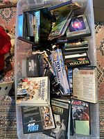 Top-down photo showing a pile of DVDs and CDs in plastic bins, titles visible include The West Wing, High House Marine, and Century of War