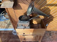 Front view of a vintage Edison hand crank gramophone showing wooden base with drawer and cabinet, metal external horn, tonearm, and turntable with vinyl record.