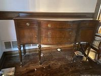 Full front view of antique Victorian sideboard showing scalloped front, three drawers, curved side cabinet doors, turned legs, dark walnut finish.