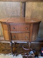Front view of the closed wooden Victorian sewing cabinet with two drawers and turned legs.