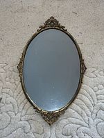Top-down shot of the antique brass mirror showing full front view and decorative brass frame details on a carpet background.