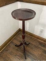 Two images showing two cherry wood plant stands with tripod legs and round tops.
