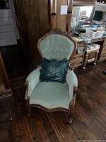 Front view of Victorian mahogany gentleman's armchair with rounded buttoned back and carved legs, upholstered in green fabric, black leather-like pillow on the seat.