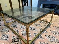 Angle view of the brass framed glass top coffee table showing the square shape and aged brass patina