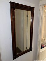 Full frontal view of the large rectangular mirror with dark wooden frame hanging on a wall next to a doorway and bathroom.