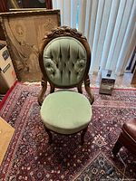 Front-facing view of Victorian Rococo carved walnut chair with green button tufted upholstery on back and seat, positioned on patterned rug indoors.