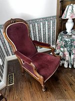 Side angle photo showing the hand carved mahogany frame, padded armrests with red velvet fabric, and wooden legs of the Victorian chair.