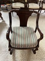 Front view of Victorian wooden rocking chair showing striped removable seat cushion and carved wooden backrest with curved armrests.