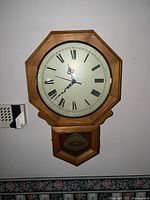 Close-up photo of one antique wooden wall clock with Roman numeral face and decorative lower panel