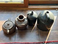 Top-down view of four pottery vessels, including two large black-glazed jugs and two brown jugs, one with a lid and one with metal handle strap.