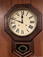 Front view showing the clock face featuring Roman numerals in an octagonal wooden frame.