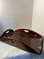 Wide angle photo showing antique wooden folding tray in partially folded position highlighting its dark wood finish, handles, and brass hinges.