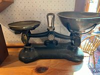 Front side view of the antique balance scale showing black cast iron base, two metal weighing pans of different sizes and central dial.