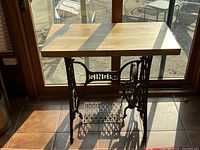 View of antique Singer sewing machine table with wood top and cast iron black base, showing metalwork and Singer logo.