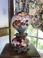 Front angle of the antique Victorian Gone With The Wind lamp showing the hand painted floral globe and ornate metal base details.