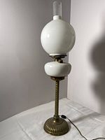 Full view of the antique Victorian oil lamp showing white glass globe, white glass reservoir, brass stem, ormolu base, and attached electric cord with switch.