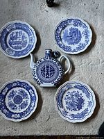 Top view of four blue and white porcelain plates arranged around one blue and white saki pitcher on carpeted floor.