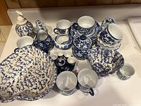 Photo of blue and white porcelain lot showing heart-shaped dishes, jars with lids, small pitchers, and various cups with blue floral and splatter patterns on white porcelain.