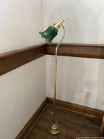 Full view of the floor lamp showing brass base, curved stand, and green glass shade.
