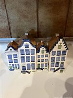 Front view of four porcelain building figurines with distinct blue and white windows and brown roofs