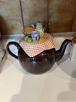 Front angle of mid-century modern ceramic teapot with a decorative lid featuring miniature food and kitchen items
