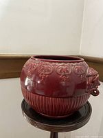 Front side view of the round red porcelain pot showing the embossed pattern and vertical ridges around the base.