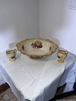 Set of three items including large wash bowl centered with a small pitcher and cup on each side on a white cloth.
