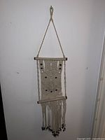 Front view of the hand knit hanging tapestry showing the geometric pattern, hanging cords, wooden dowels, and fringe with beads.