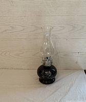 Black flower lantern with clear chimney flute, showing floral decoration on the base and clear chimney flute, against a light wood background.