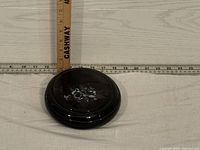 Top and side view of closed black pottery dish with white floral design on lid and a ruler showing about 4 inch diameter