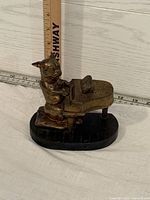 Front-right angle of brass dog playing piano figurine with ruler behind indicating size.