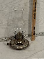 Photo showing silver-tone oil lantern with clear glass chimney and measurement scale indicating about 12 inches tall.