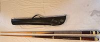 Two assembled pool cues and black carrying case laid out on a white surface
