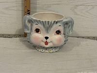 Front and slightly angled view of a ceramic puppy dog shaped bowl showing detailed painted features, ears, and polka dot collar.
