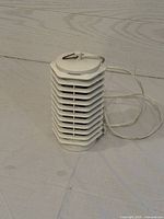 White electric bug zapper on flat surface with visible vented design and power cord attached.